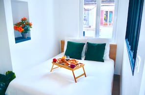 Ein Bett mit einem Frühstücksbrett, ein Fenster mit Blick und ein Blumentopf an der Wand.