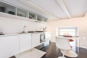 A modern kitchen with white cabinets, a stove, and a dining area with a white chair and table. - Fori Imperiali Hi Tech Apartment (Roma)