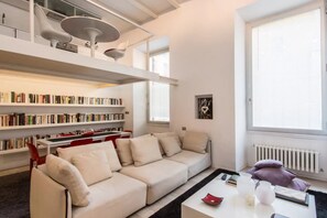 A modern living room with a sofa, a coffee table, and bookshelves filled with books. - Fori Imperiali Hi Tech Apartment (Roma)