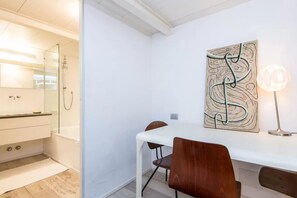 A modern bathroom with a shower, a white sink, and a mirror. There is a white table with two chairs and a wall-mounted abstract art piece. - Fori Imperiali Hi Tech Apartment (Roma)