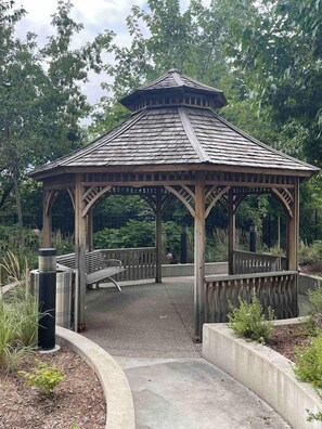 A wooden gazebo with a sloped roof, surrounded by a concrete walkway and benches. - Urban Furnished 1-BR | GTA Skyline views | Casino (Toronto)