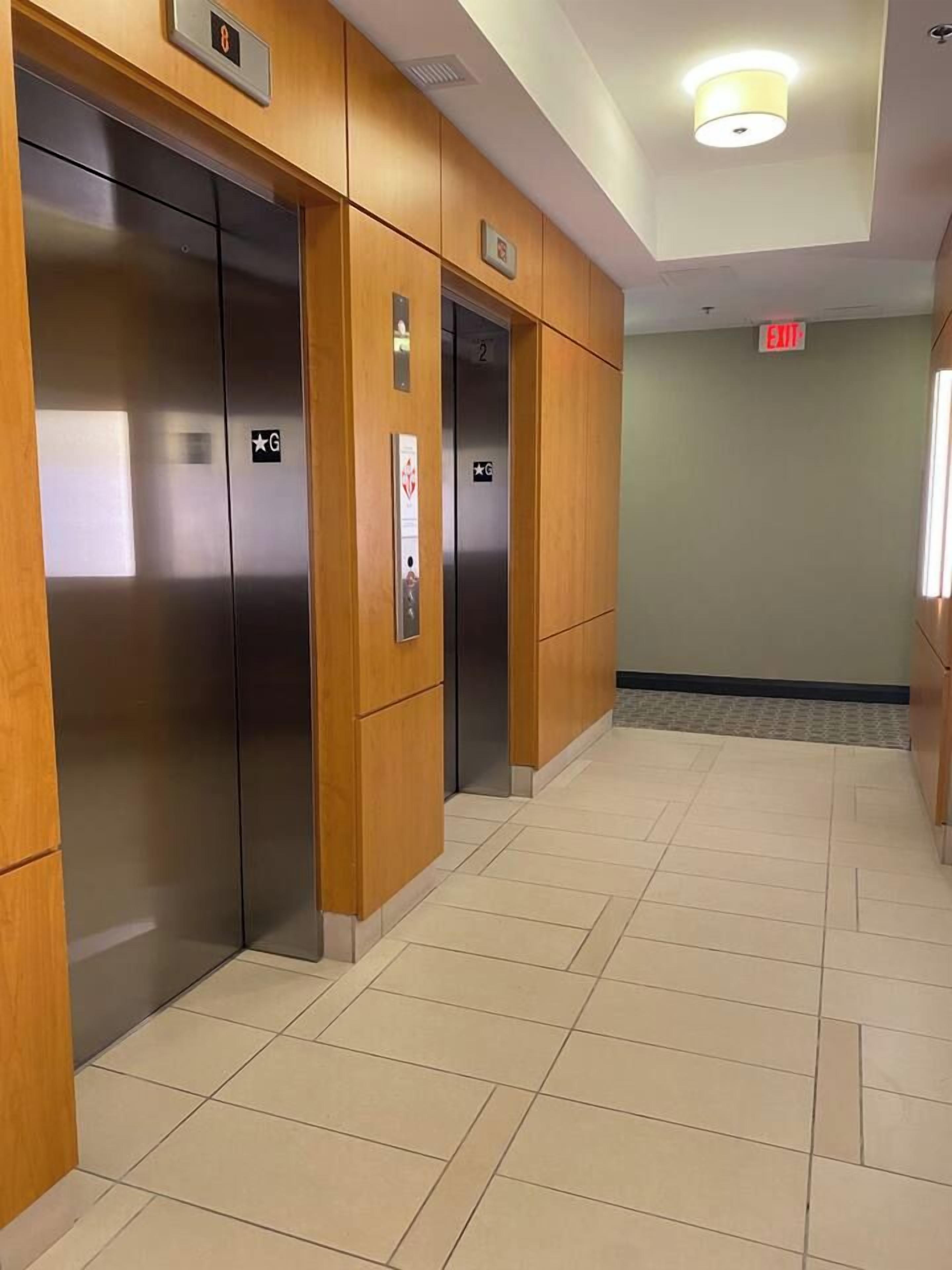A hallway with two elevators, wooden paneling, and a tiled floor.
