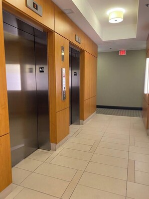A hallway with two elevators, wooden paneling, and a tiled floor. - Urban Furnished 1-BR | GTA Skyline views | Casino (Toronto)