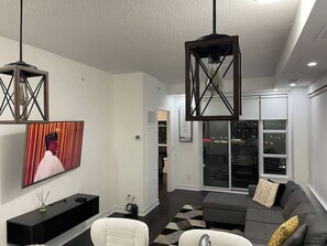 A modern living room with a flat-screen TV, a sofa, a coffee table, and a pendant light fixture. - Urban Furnished 1-BR | GTA Skyline views | Casino (Toronto)