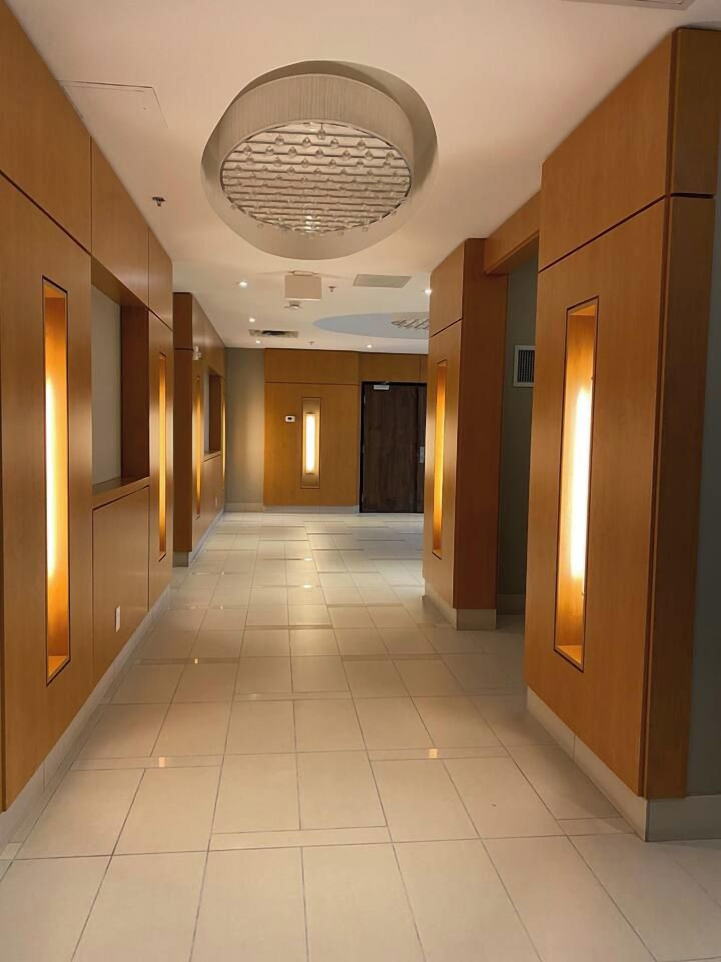 A hotel corridor with wooden paneling, recessed lighting, and a circular ceiling feature.