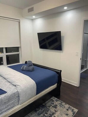 A bedroom with a bed, a flat-screen TV mounted on the wall, and a window with blinds. - Urban Furnished 1-BR | GTA Skyline views | Casino (Toronto)