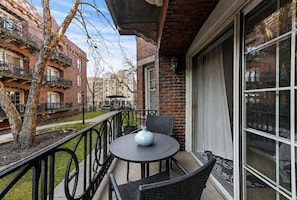 A balcony with a round table and chairs, a potted plant, and a view of neighboring buildings. - Pleasant 2BR/2BA Condo in Hyde Park (Chicago)