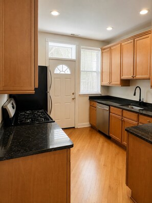 A kitchen with wooden cabinets, a black countertop, a stove, a dishwasher, and a window with blinds. - Pleasant 2BR/2BA Condo in Hyde Park (Chicago)