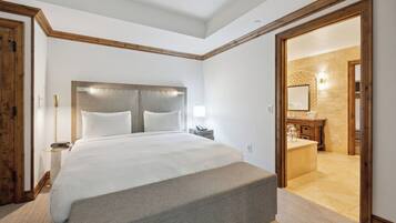 Une chambre d’hôtel avec un grand lit, une table de chevet avec une lampe et une porte en bois donnant accès à la salle de bain.