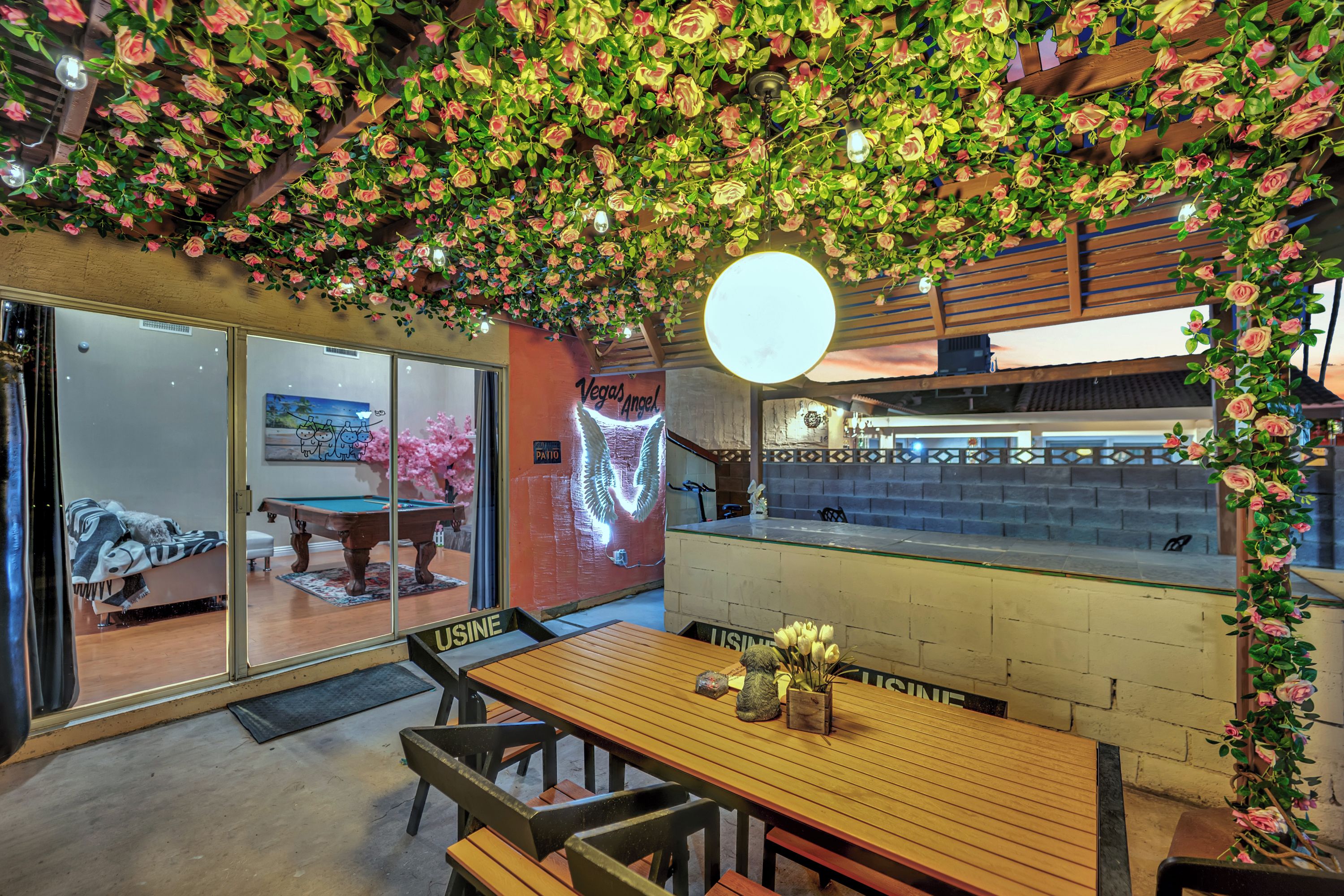 A cozy indoor space with a wooden table, chairs, and a wall adorned with artificial flowers.