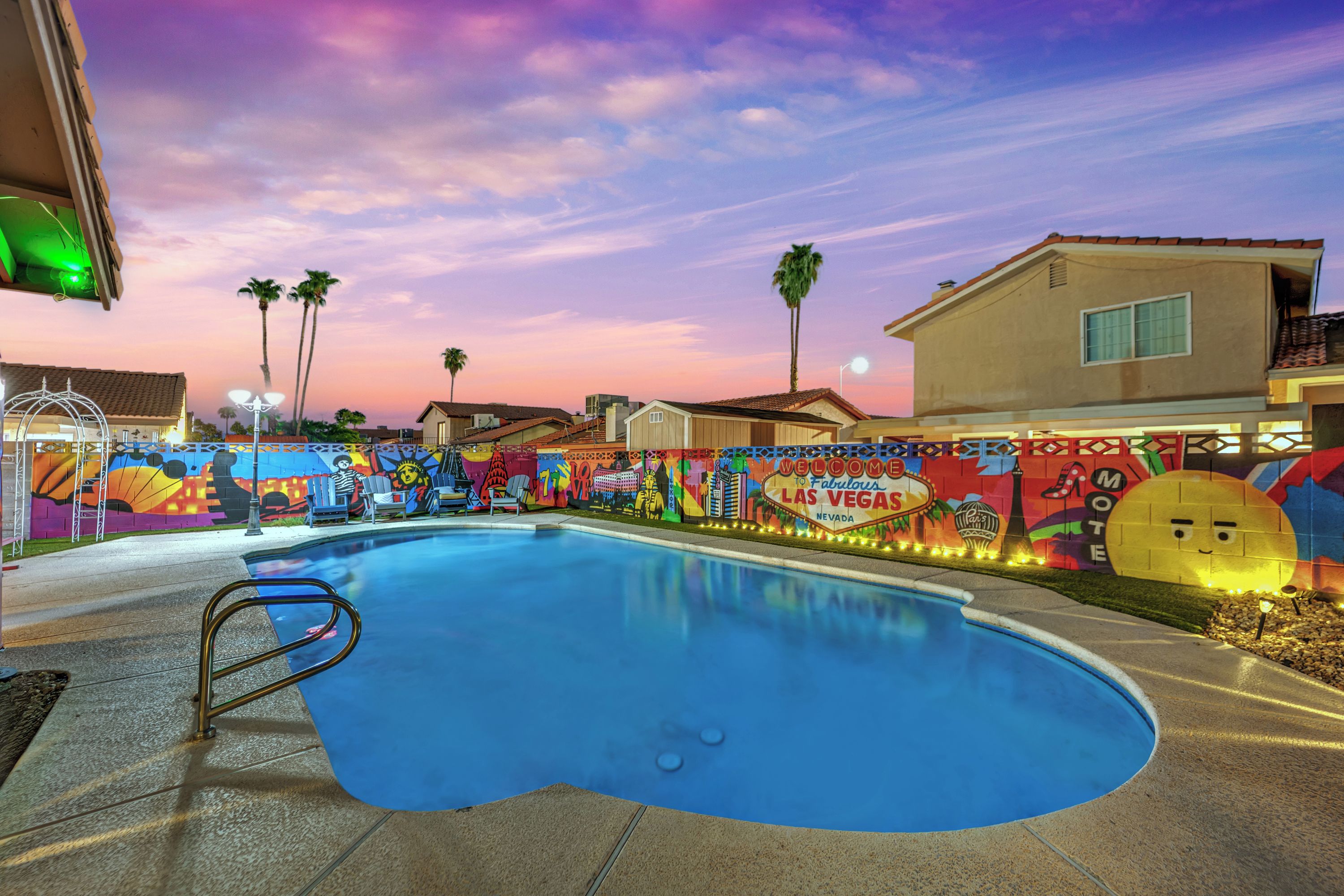 A swimming pool with a colorful mural in the background, a clear sky, and a building with a balcony.
