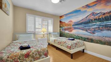 A bedroom with two beds, a nightstand, a lamp, and a large scenic wall mural.