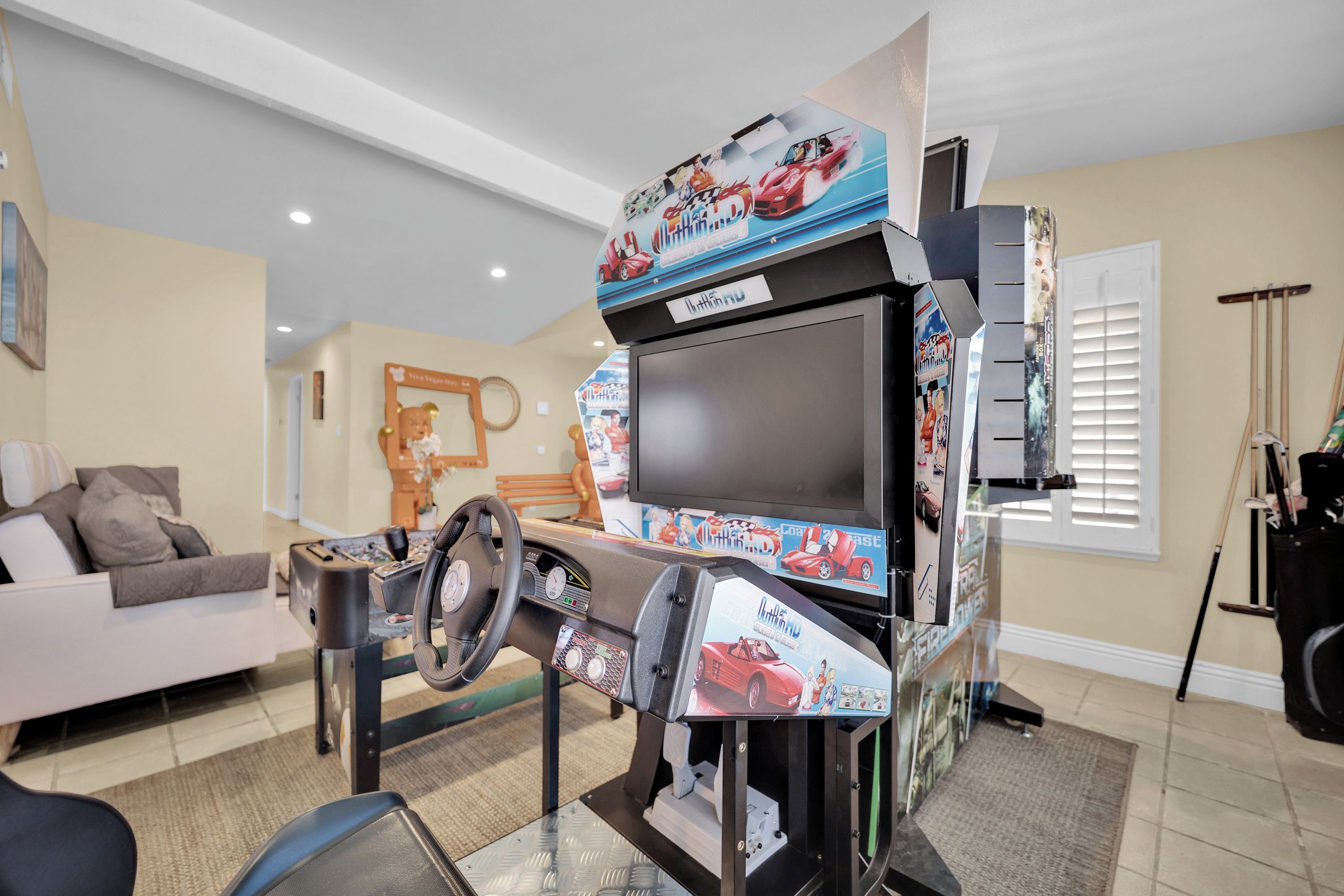 A room with a racing simulator setup, a sofa, and a window with blinds.