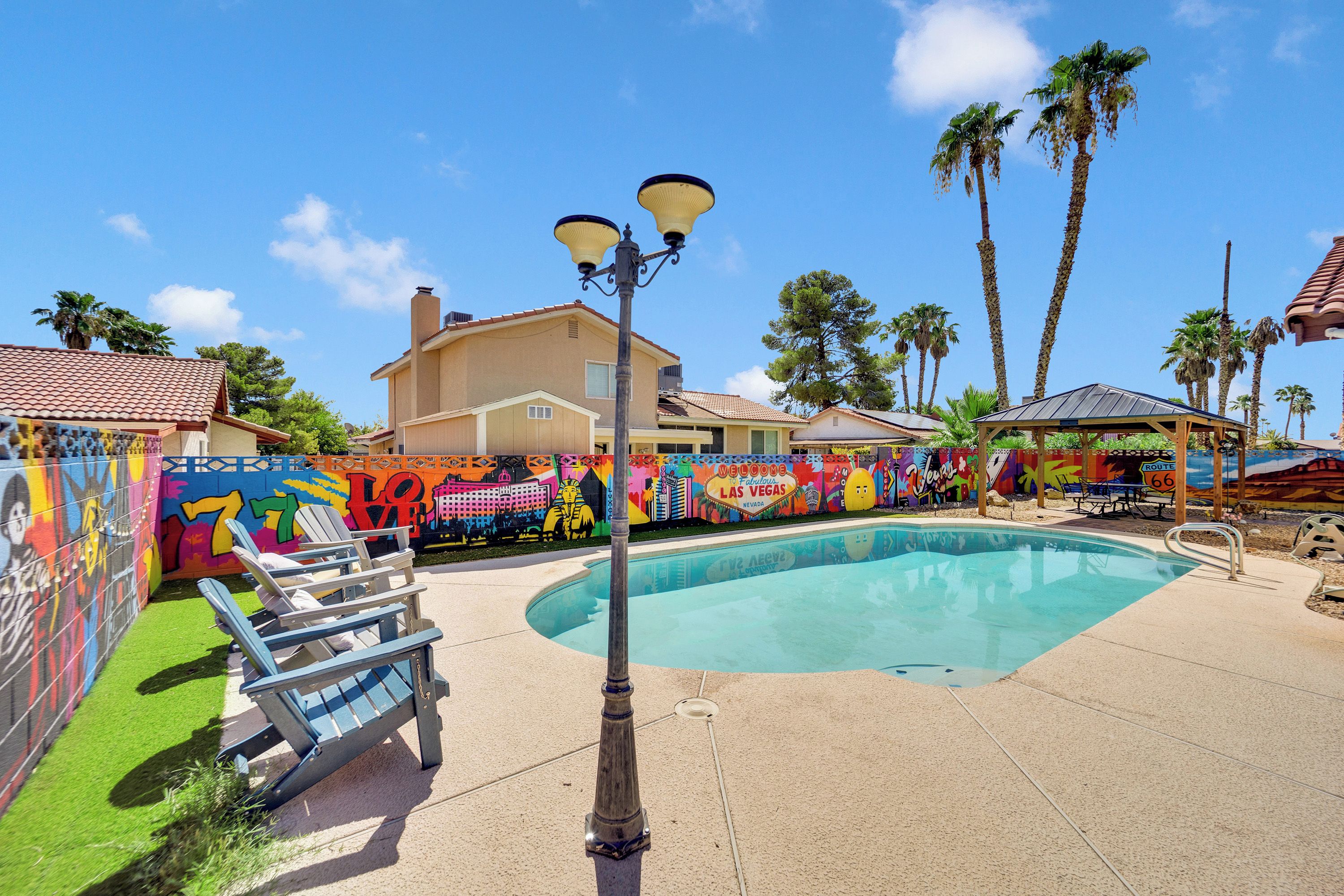 A pool area with a mural, lounge chairs, and a house in the background.