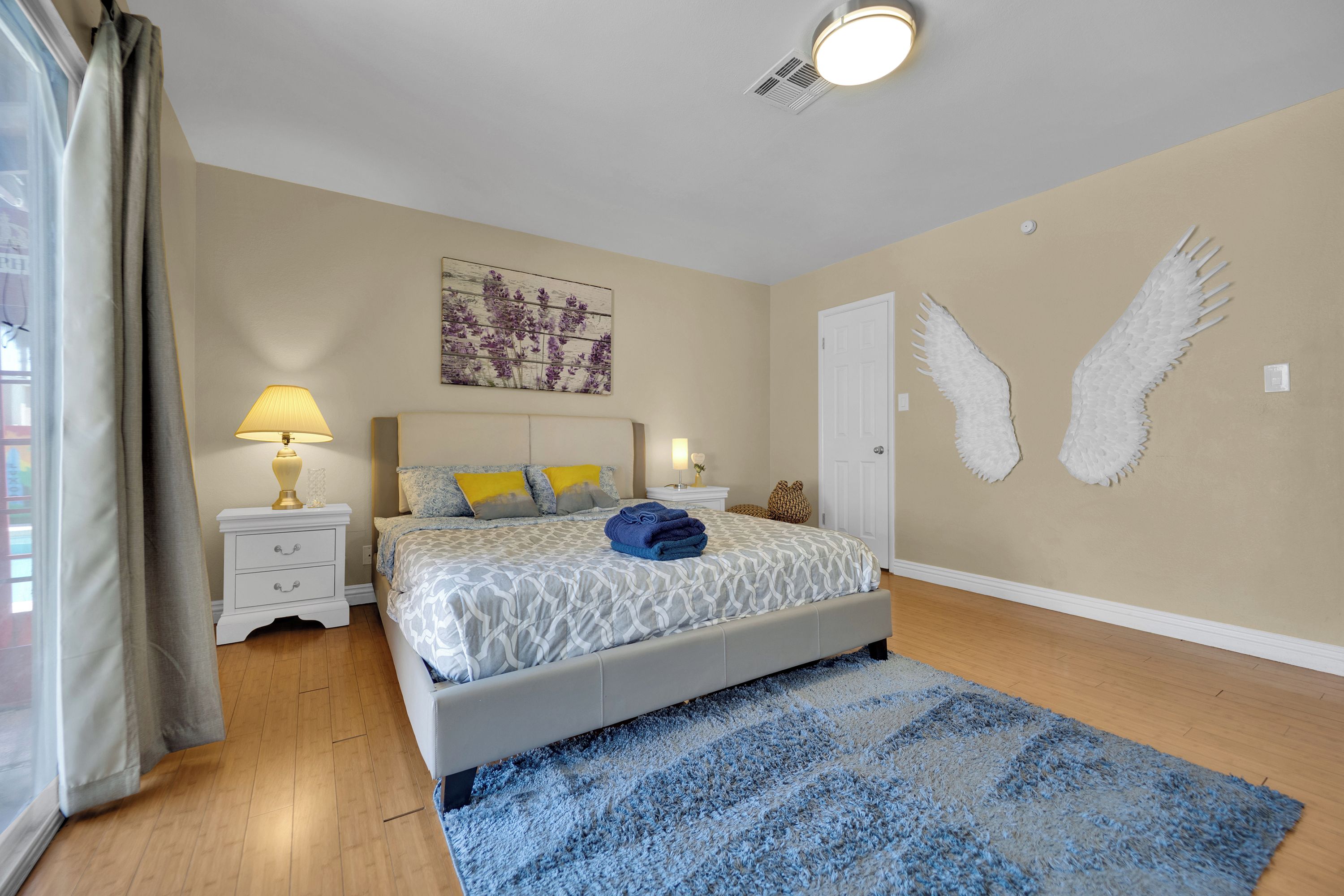 A bedroom with a bed, nightstands, a lamp, a wall art piece, and a door.