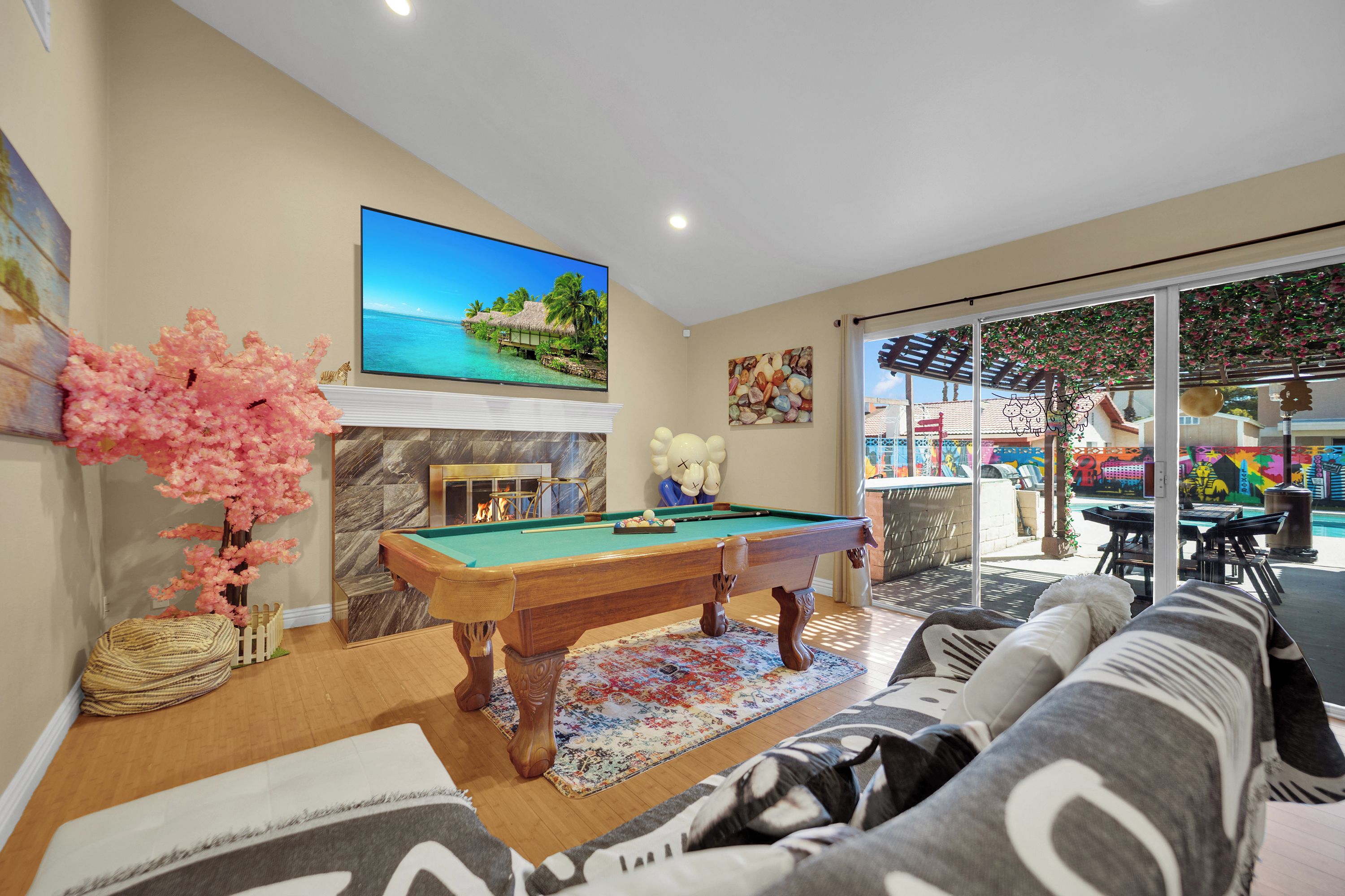 A living room with a pool table, a sofa, a fireplace, and a television displaying a tropical scene.