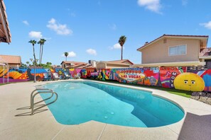 A swimming pool with a colorful mural, palm trees, and a house in the background. - Vegas Angel • Pool, Arcade Room & Strip Views (Las Vegas)