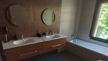 A modern bathroom with two sinks, a large mirror, and a bathtub.