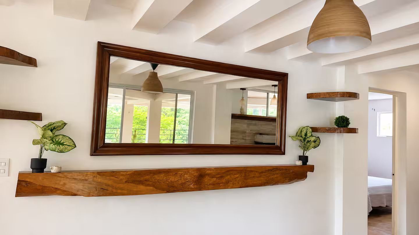 Una habitación con un espejo grande, repisa de madera y lámpara colgante.