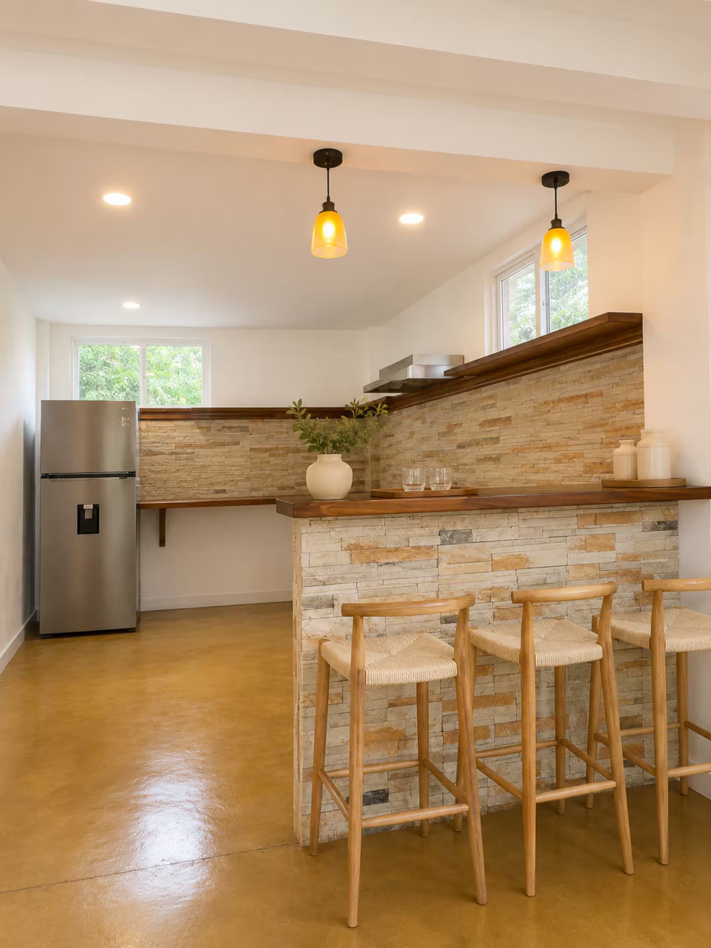 A modern kitchen with a stone backsplash, wooden bar stools, and a stainless steel refrigerator.
