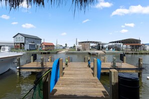 A wooden dock leading to a marina with boats, a house, and a covered area. - The Treasure Hunter In Water Docked Studio Boat (Bay City)