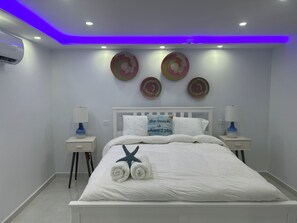 A modern bedroom with a white bed, two bedside tables with lamps, decorative wall art, and a ceiling with blue LED lighting. - Caribe House, just 7 minutes from the San Juan airport, close to everything (Carolina)