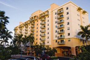 A multi-story hotel with balconies, palm trees, and a parking area. - Pompano Beach | Pool & Golf Access | Coastal Escape Stay (Pompano Beach)