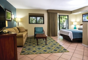 A hotel room with a bed, a sofa, a chair, a desk, a TV, and a window with curtains. - Pompano Beach | Pool & Golf Access | Coastal Escape Stay (Pompano Beach)
