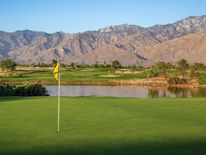 Een golfbaan met een vlag, een vijver en bergen op de achtergrond.