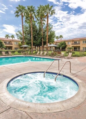 A hot tub surrounded by lounge chairs, palm trees, and a pool in a resort setting. - Palm Springs | Easy Access Studio Stay | Pool + Spa (Cathedral City)