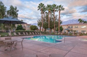 A pool area with lounge chairs, a table, and umbrellas. - Palm Springs | Easy Access Studio Stay | Pool + Spa (Cathedral City)