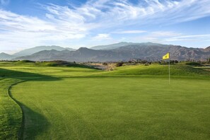 A golf course with a flag, rolling hills, and mountains in the background.