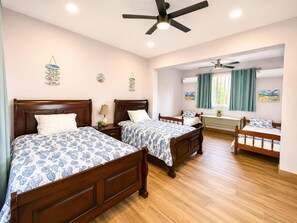 A hotel room with two wooden beds, a ceiling fan, a window with curtains, and a wall-mounted air conditioner.
