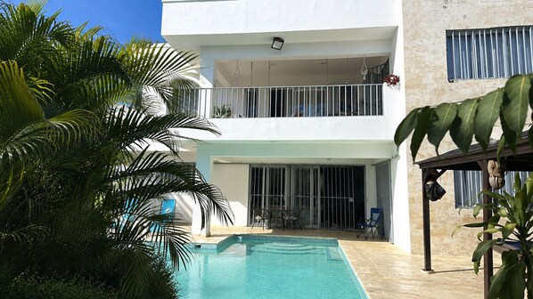 A two-story building with a swimming pool, outdoor furniture, and a covered patio area.