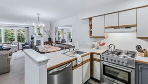 A modern kitchen with a central island, stainless steel appliances, and a dining area with a fireplace. - Okemo Ski Escape | Steps to the Slopes (Ludlow)