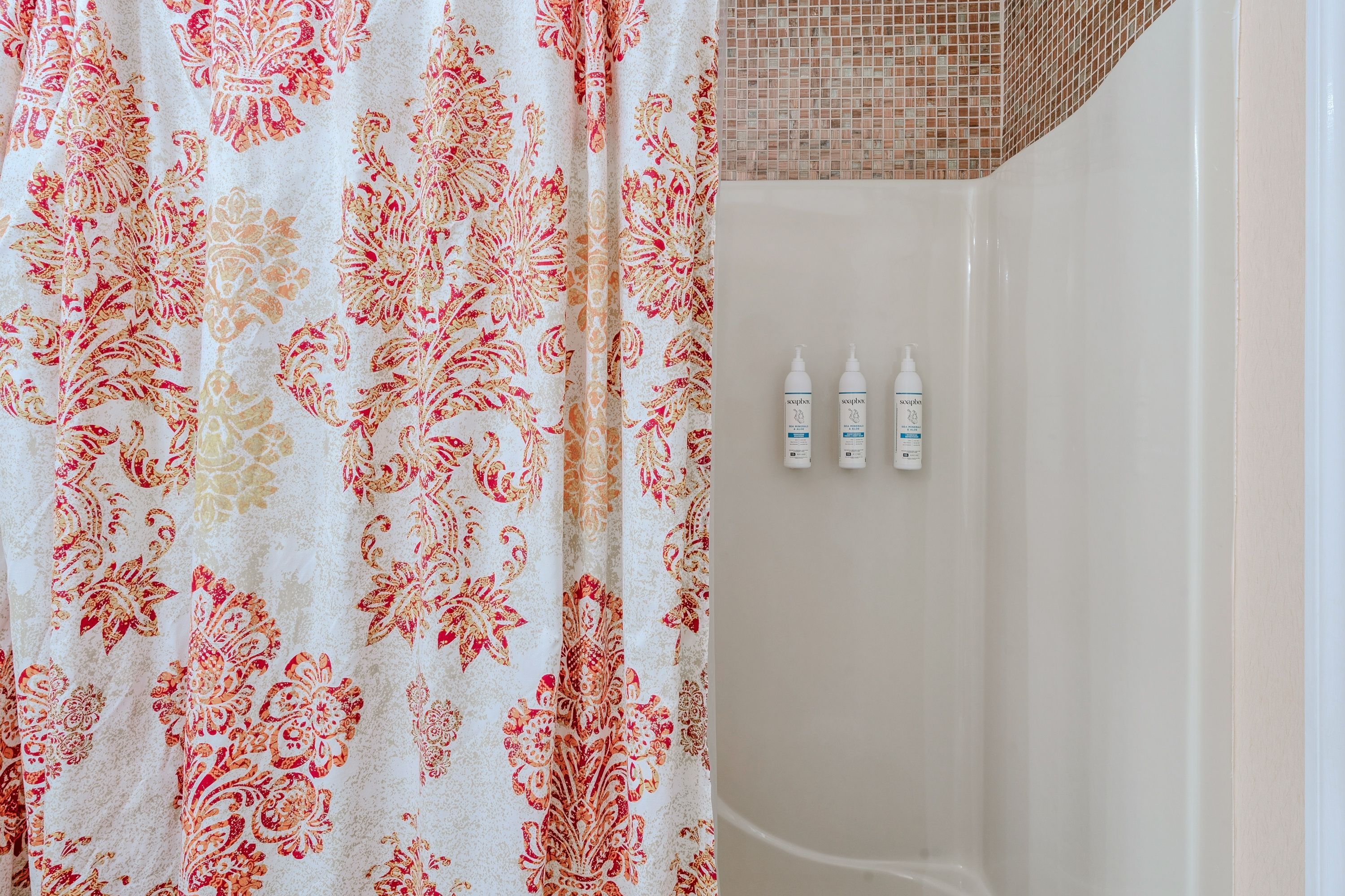 Une salle de bain avec un rideau de douche à motifs, un mur carrelé et trois bouteilles de savon.