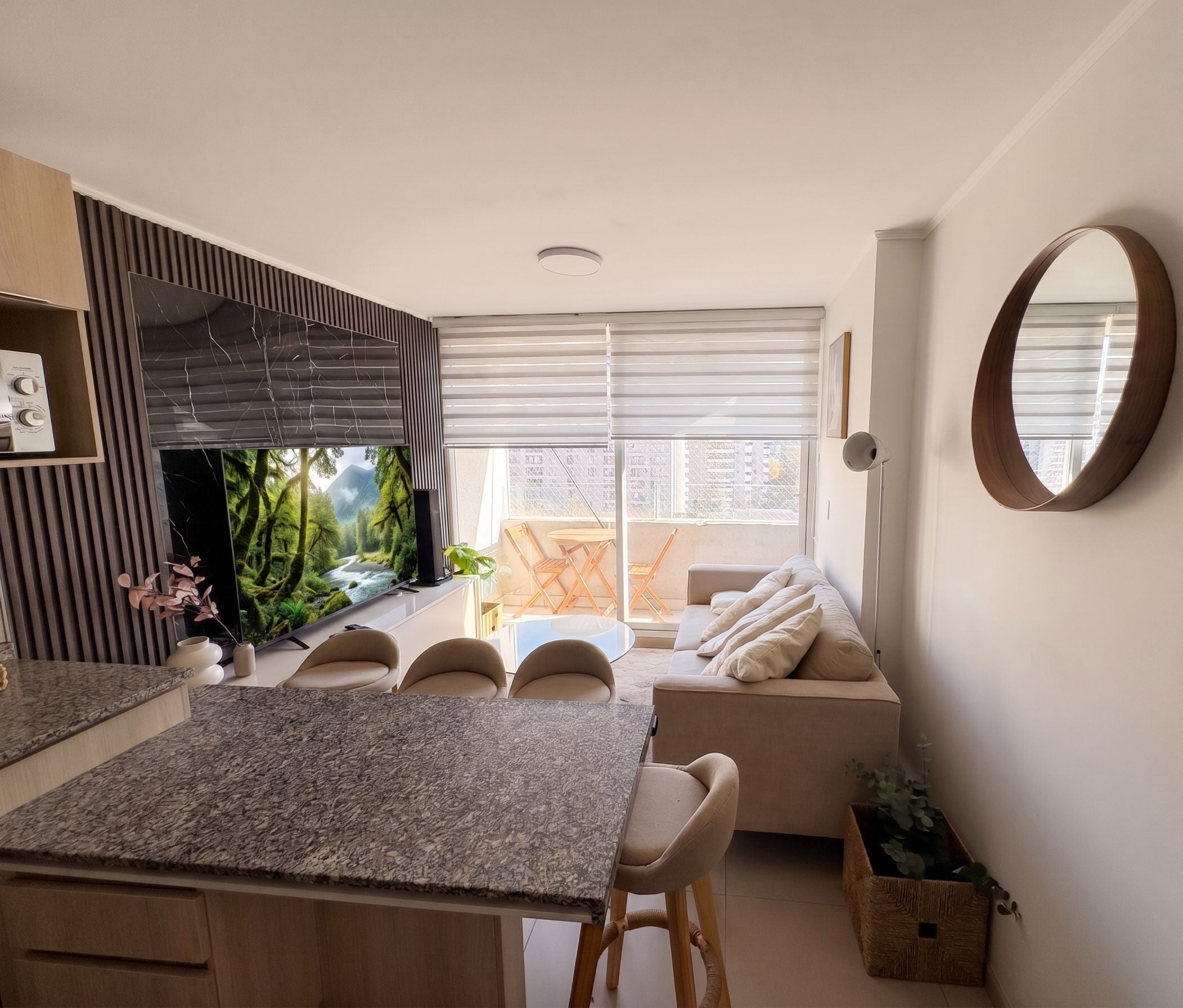 A modern kitchen with a central island, a dining area with a sofa, and a large window with blinds.