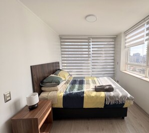 Een slaapkamer met een bed, nachtkastje en een raam met zonwering.