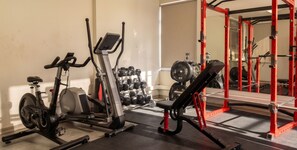 Een sportschool met trainingsapparatuur, waaronder een hometrainer, een bankdrukpers en een squatrek.