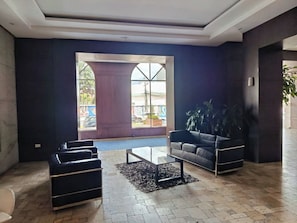 A lobby with a large arched window, a black leather sofa, a glass coffee table, and a potted plant. - LUXURY SUITE, Comfortable and Fully Furnished (Quito)