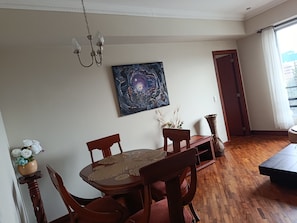 A dining area with a wooden table and chairs, a painting on the wall, and a view through an open door. - LUXURY SUITE, Comfortable and Fully Furnished (Quito)