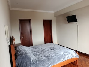 A bedroom with a bed, two doors, a wall-mounted TV, and a telephone. - LUXURY SUITE, Comfortable and Fully Furnished (Quito)