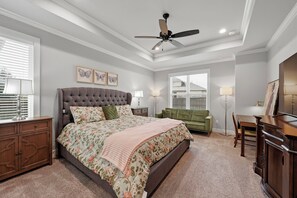 A bedroom with a large bed, a ceiling fan, a green sofa, and a desk with a lamp.
