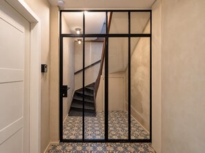 A hallway with a tiled floor leading to a staircase with a black railing. - Stylish 2BR Hotel Room | Heart of Le Sablon (Brussels)
