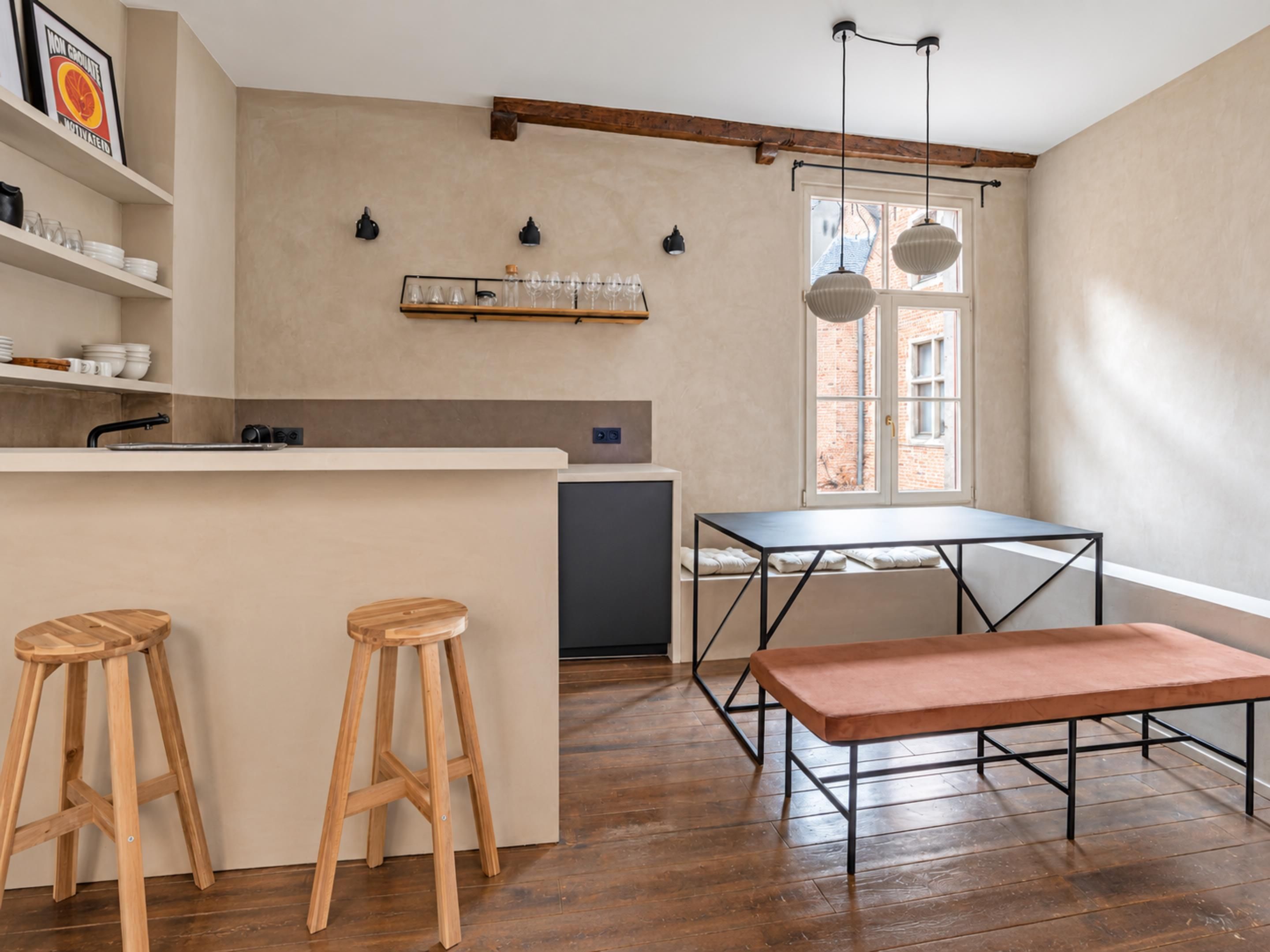 Een keuken met houten krukken, een bank, hanglampen en een raam met uitzicht.