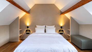 A bedroom with a large bed, two bedside tables with lamps, a bench, and exposed wooden beams.
