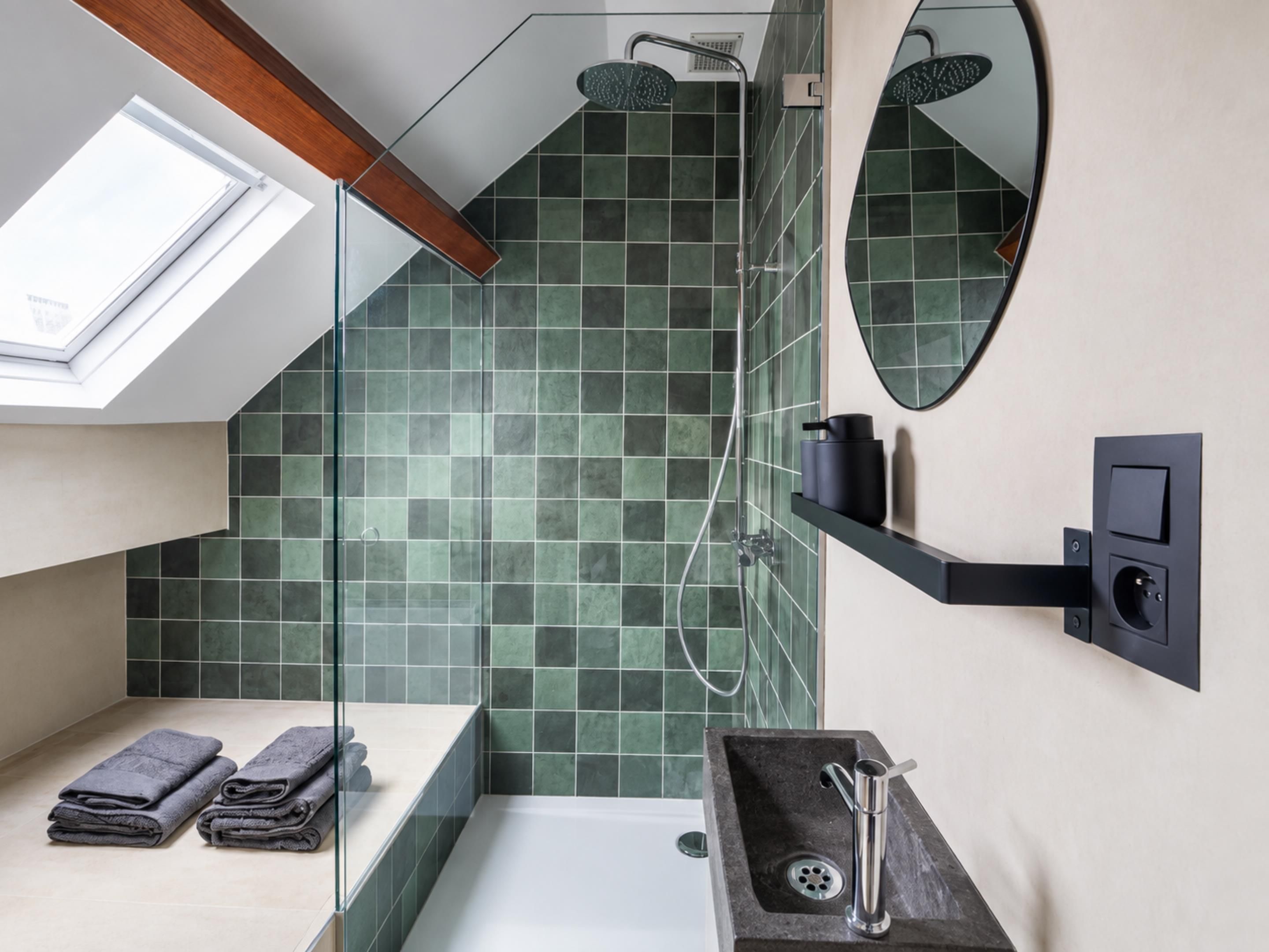 Een moderne badkamer met dakraam, douche, wastafel en spiegel.