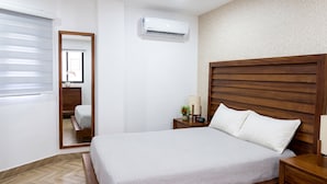 Une chambre d’hôtel comprenant un lit, une table de chevet avec une lampe, une petite table avec une horloge, un miroir et un appareil de climatisation.