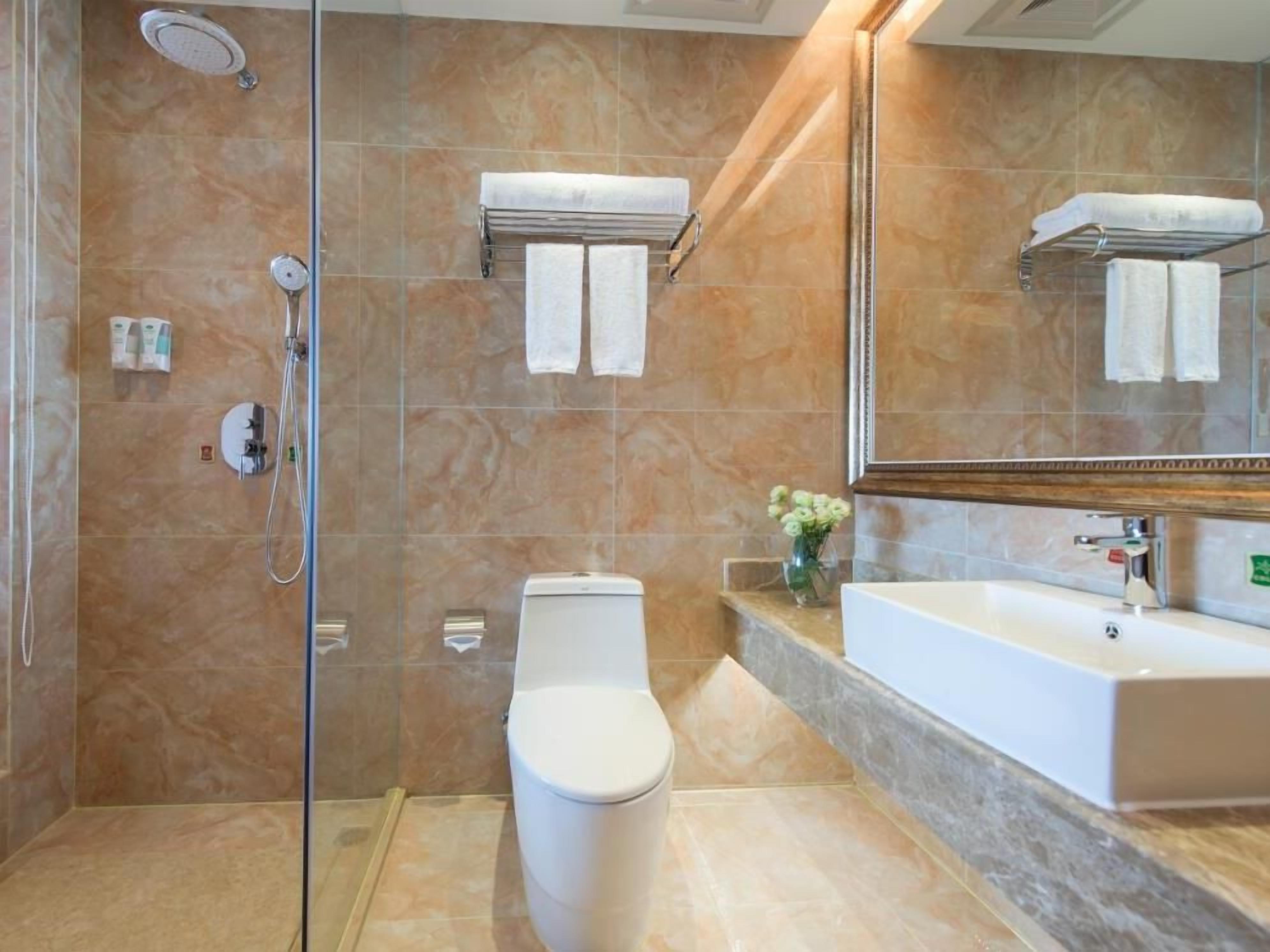A bathroom with a glass-enclosed shower, a toilet, a sink, and a mirror.