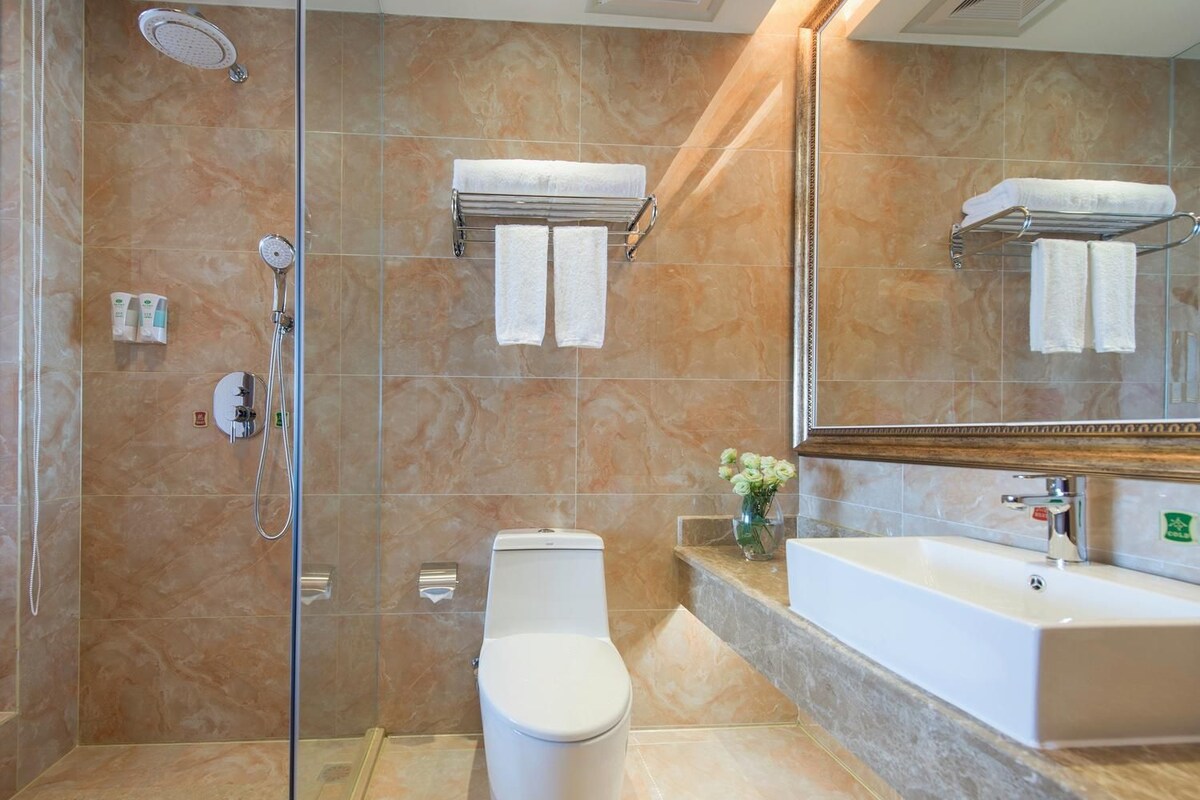 Ein modernes Badezimmer mit Duschkabine aus Glas, Toilette, Waschbecken mit Spiegel und einer Vase mit Blumen auf der Ablagefläche.